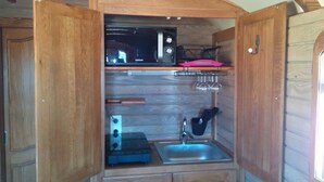 A compact kitchenette with a microwave, a sink, and a small countertop. - Roulotte La Nanouche (Le Cailar)