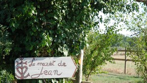 A wooden sign with a white background and red lettering, partially obscured by green foliage. - Roulotte La Nanouche (Le Cailar)