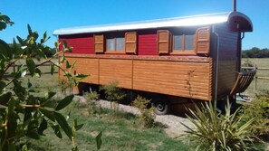 A stationary wooden train car with a red exterior and windows, situated in a grassy area. - Roulotte La Nanouche (Le Cailar)