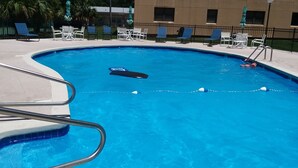 A swimming pool with lounge chairs and umbrellas, surrounded by a fence and a building in the background. - Beauvoir (Beautiful View) (Biloxi)