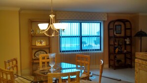A dining area with a table and chairs, a chandelier, and a window with blinds. - Beauvoir (Beautiful View) (Biloxi)