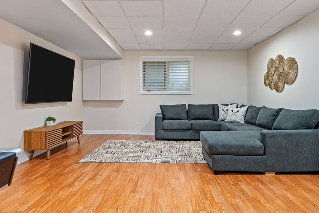 A modern living room with a sectional sofa, a flat-screen TV, a wooden cabinet, and a patterned rug.