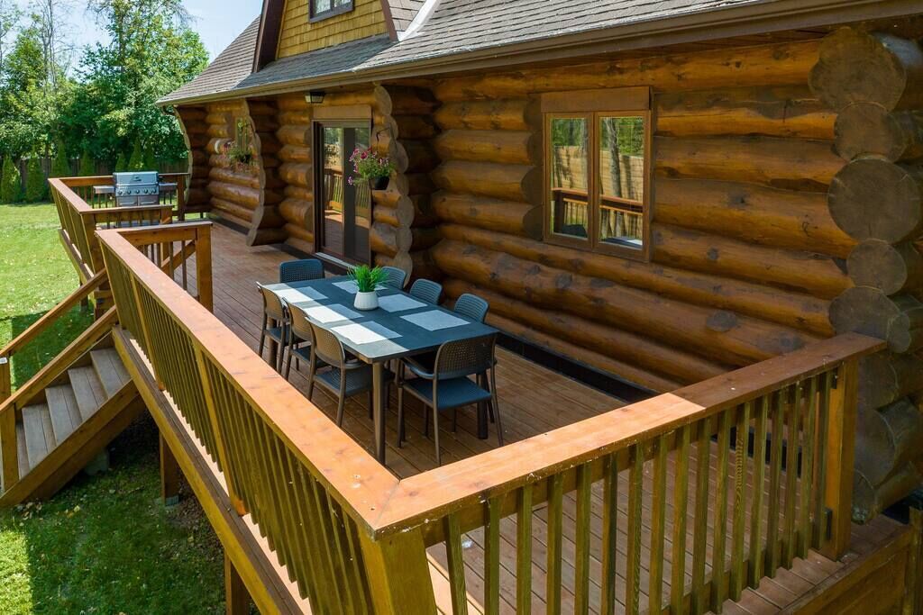 A log cabin with a deck, outdoor seating, and a grill.