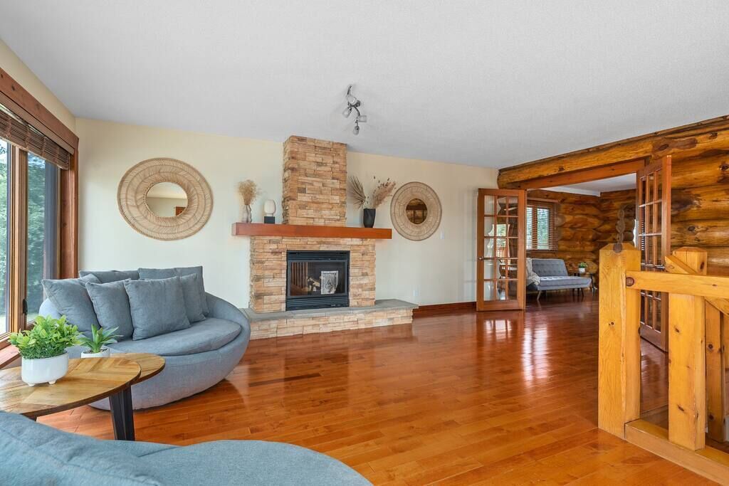 Un salon spacieux avec une cheminée en pierre, un canapé gris et un plancher en bois.