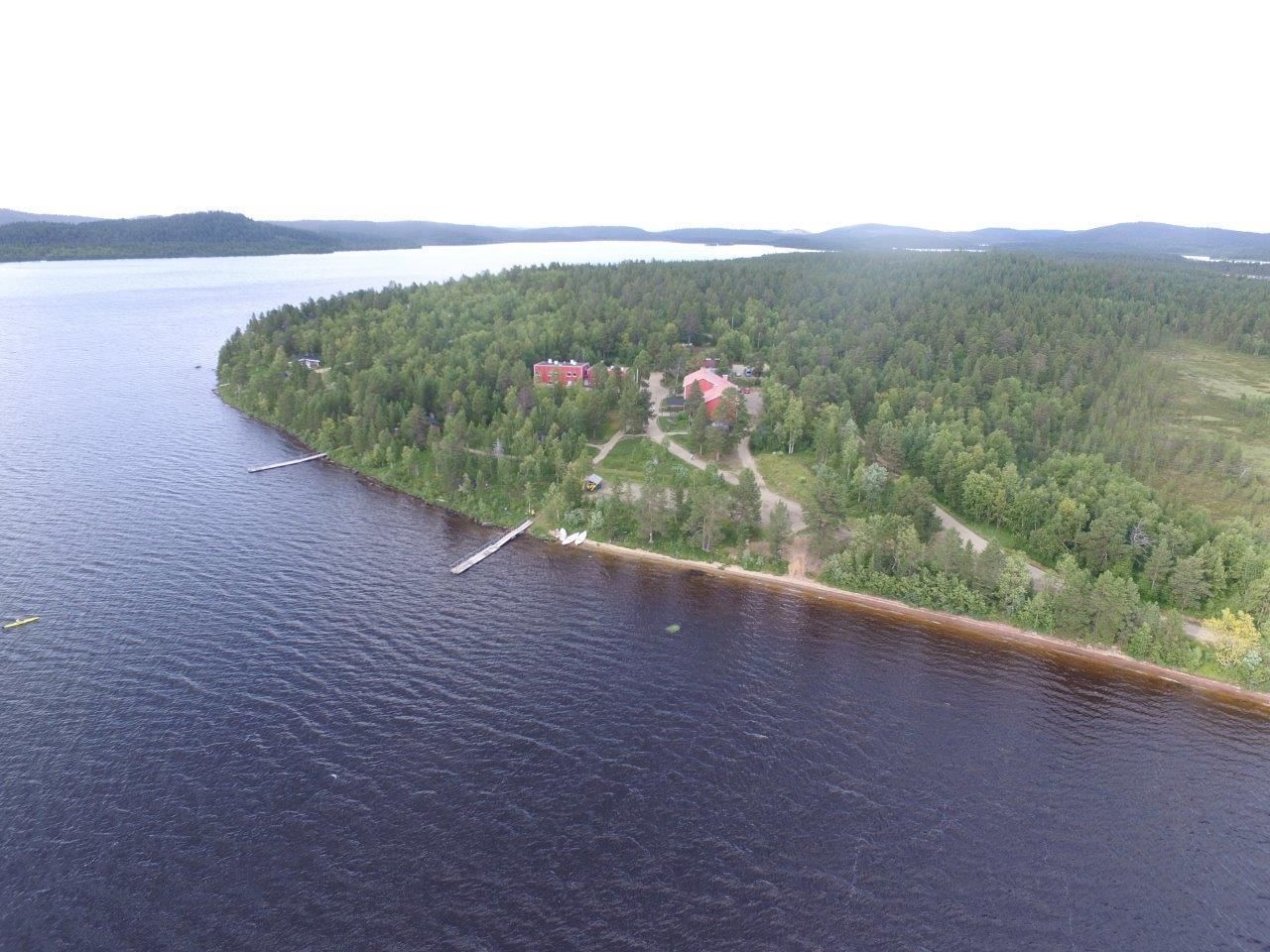 An aerial view of a lakeside property with a dock, a small building, and a forested area.