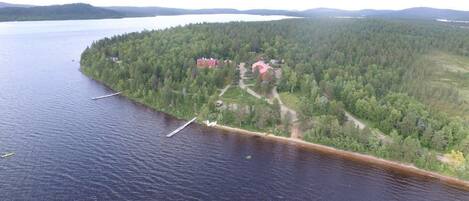 An aerial view of a lakeside property with a dock, a small building, and a forested area.