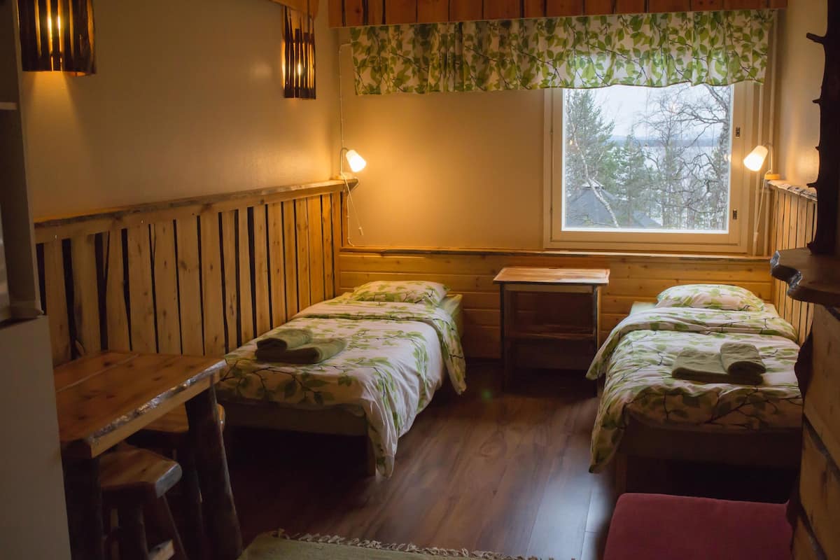 A cozy room with two wooden beds, a small table, and a window with a view of trees.