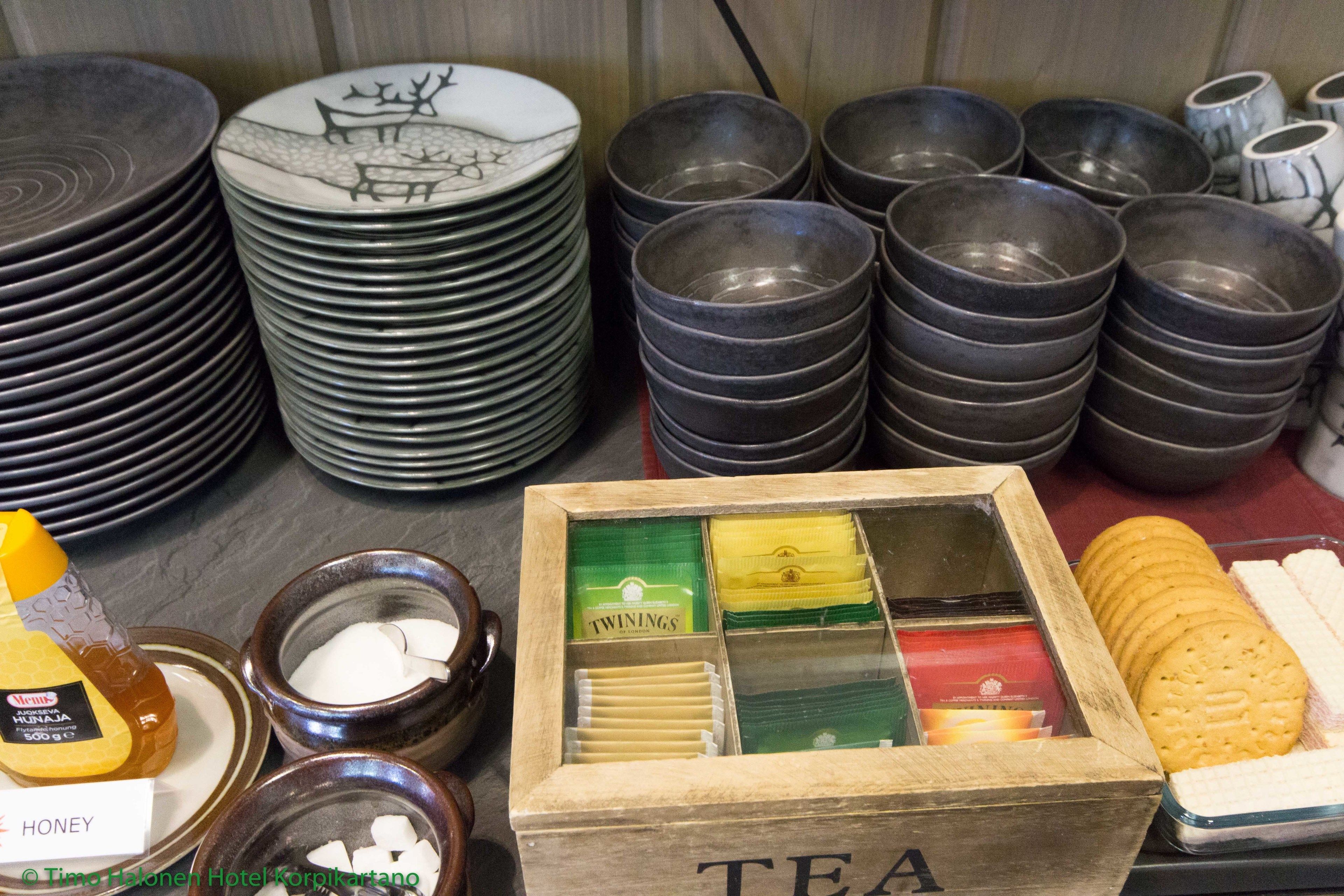 Stacks of plates and bowls, a wooden box labeled "TEA", and a honey jar.