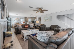 A spacious living room with a large leather sofa, a coffee table, and a dining area with a kitchen in the background.