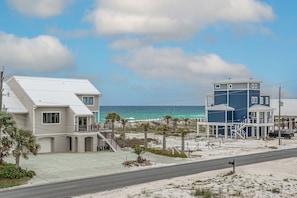 A coastal property with a two-story house and a separate building, both featuring balconies and a view of the ocean.
