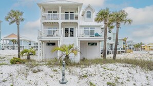 Ein mehrstöckiges Strandhaus mit Balkonen, einer Garage und einem Sandstrand im Vordergrund.