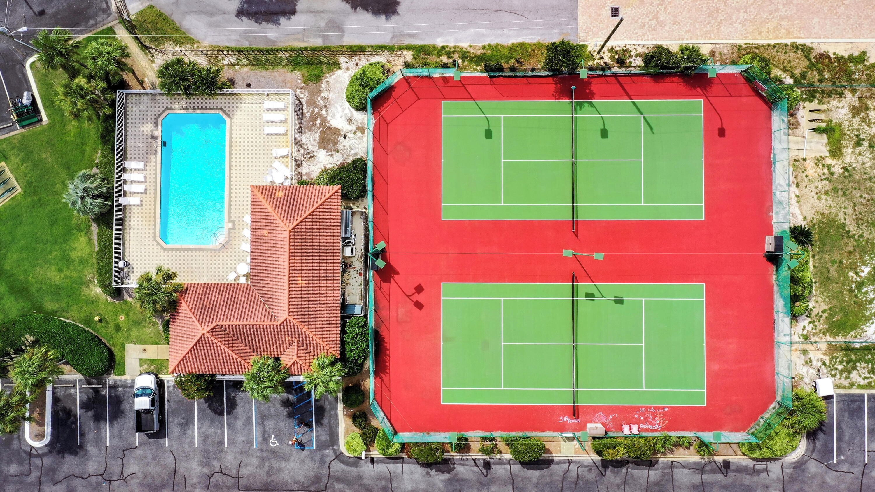 An aerial view of a property with a swimming pool, tennis courts, and a parking area.