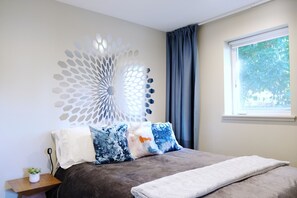 A bedroom with a bed, a decorative wall piece, a window with curtains, and a small plant on a nightstand.