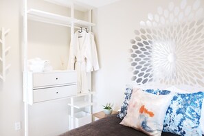 Quarto com cama, guarda-roupa branco, espelho e um objeto decorativo na parede.