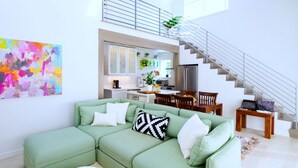 Ein modernes Wohnzimmer mit einem grünen Ecksofa, einer Treppe und einer Küche im Hintergrund.