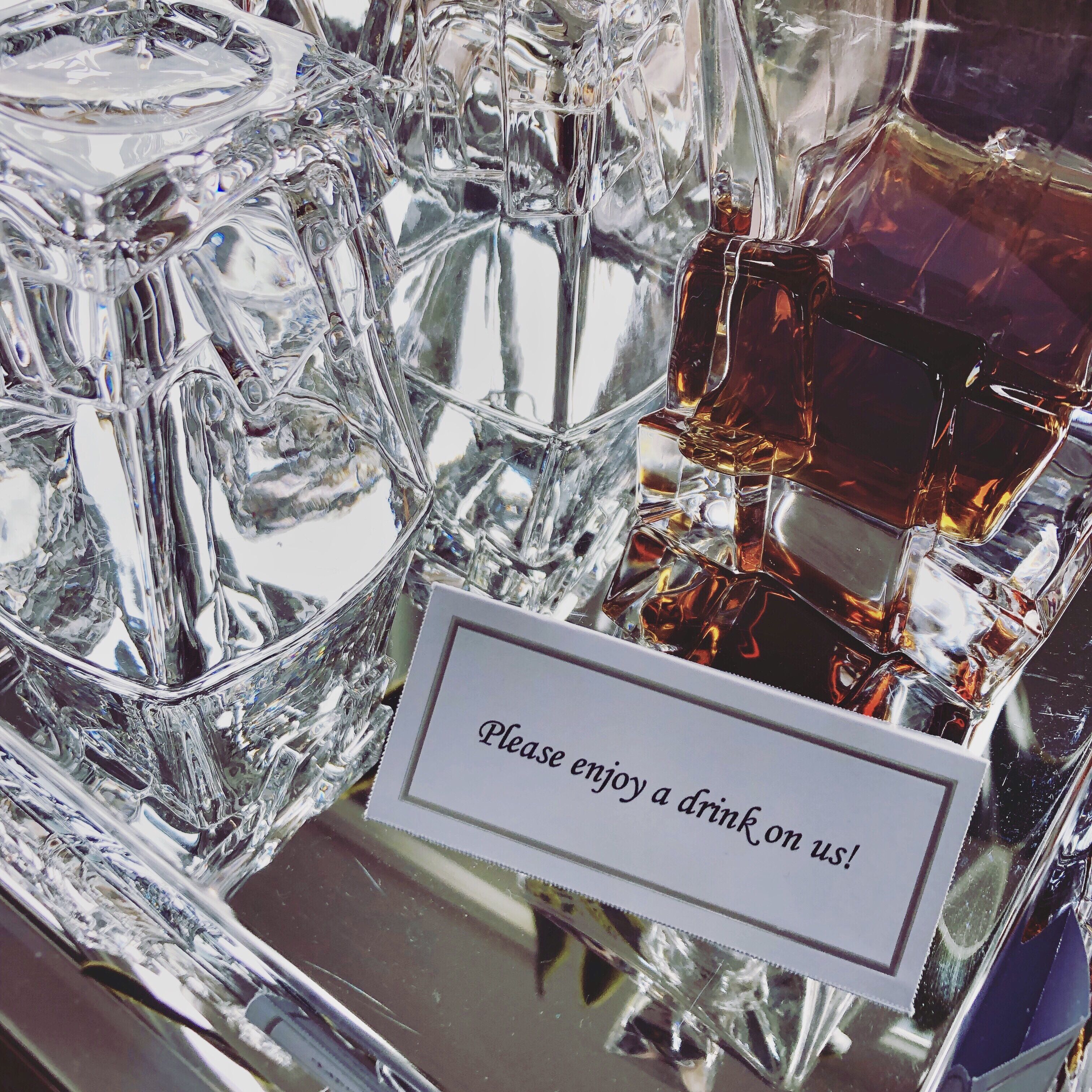 Recipiente de vidro com uma placa que diz 'Desfrute de uma bebida por nossa conta!'