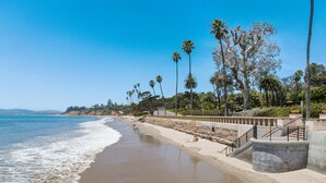 A beach with a concrete walkway, palm trees, and a clear blue sky.