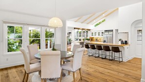 A modern kitchen with a central island, wooden flooring, and large windows offering a view of greenery.