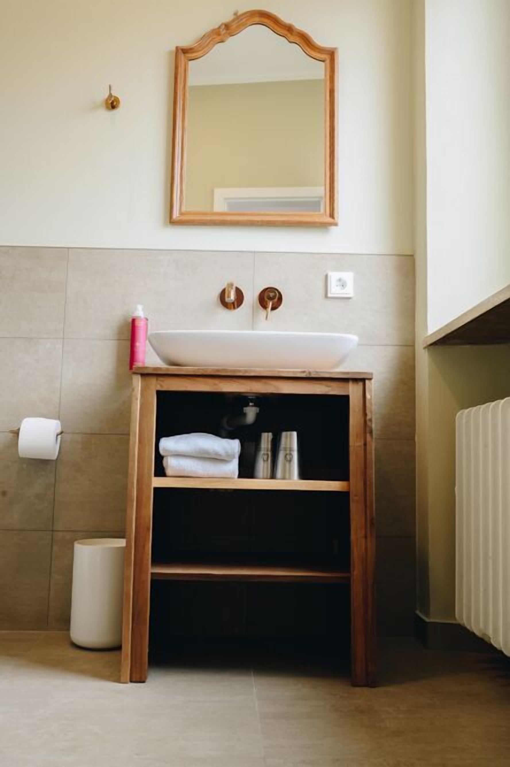 Ein Badezimmer mit einem Holzkosmetikschrank, einem weißen Waschbecken, einem Spiegel und einem Handtuchhalter.