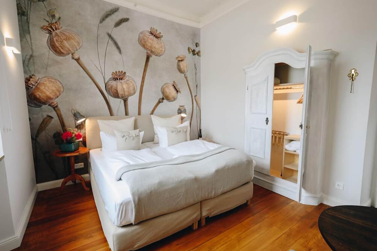 Une chambre à coucher avec un grand lit, une table de chevet avec une lampe, une fresque murale et une armoire.