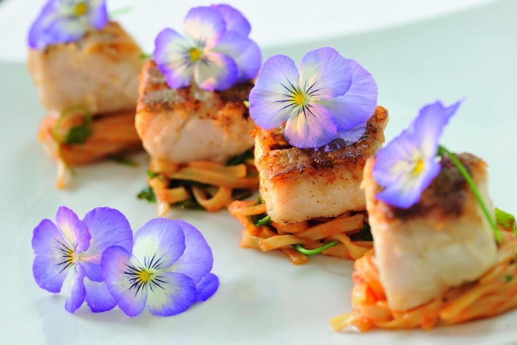 A dish with seared fish and purple flowers on a white plate.