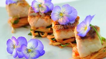 A dish with seared fish and purple flowers on a white plate.