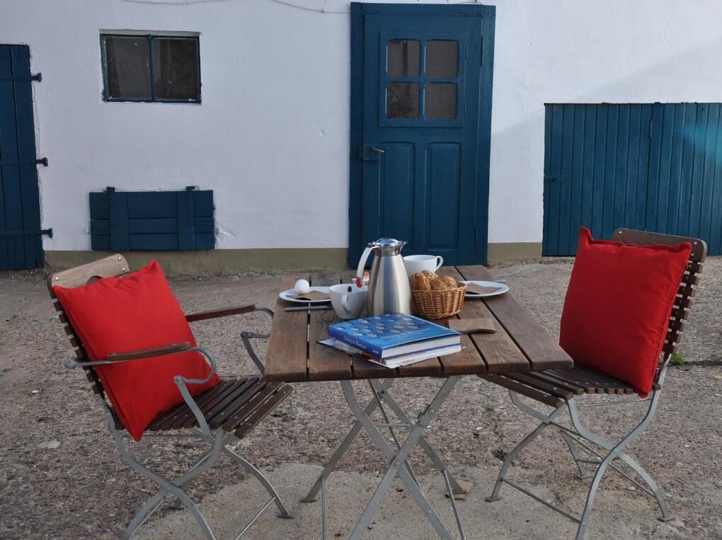 A rustic outdoor seating area with a wooden table, metal chairs, and a blue door in the background.