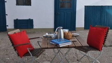 A rustic outdoor seating area with a wooden table, metal chairs, and a blue door in the background.