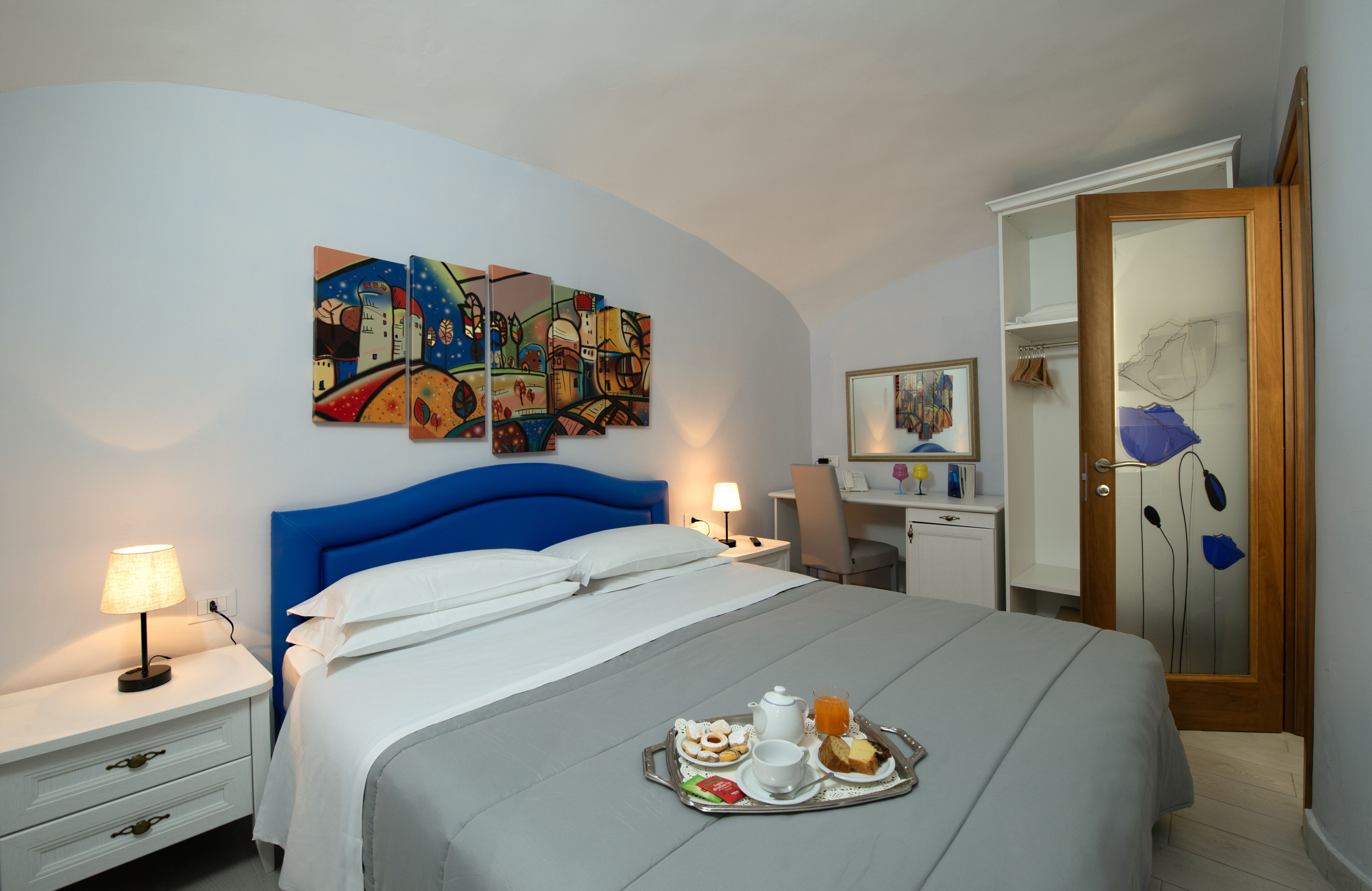 Una habitación de hotel con una cama, una bandeja de desayuno, un escritorio y un cuadro en la pared.