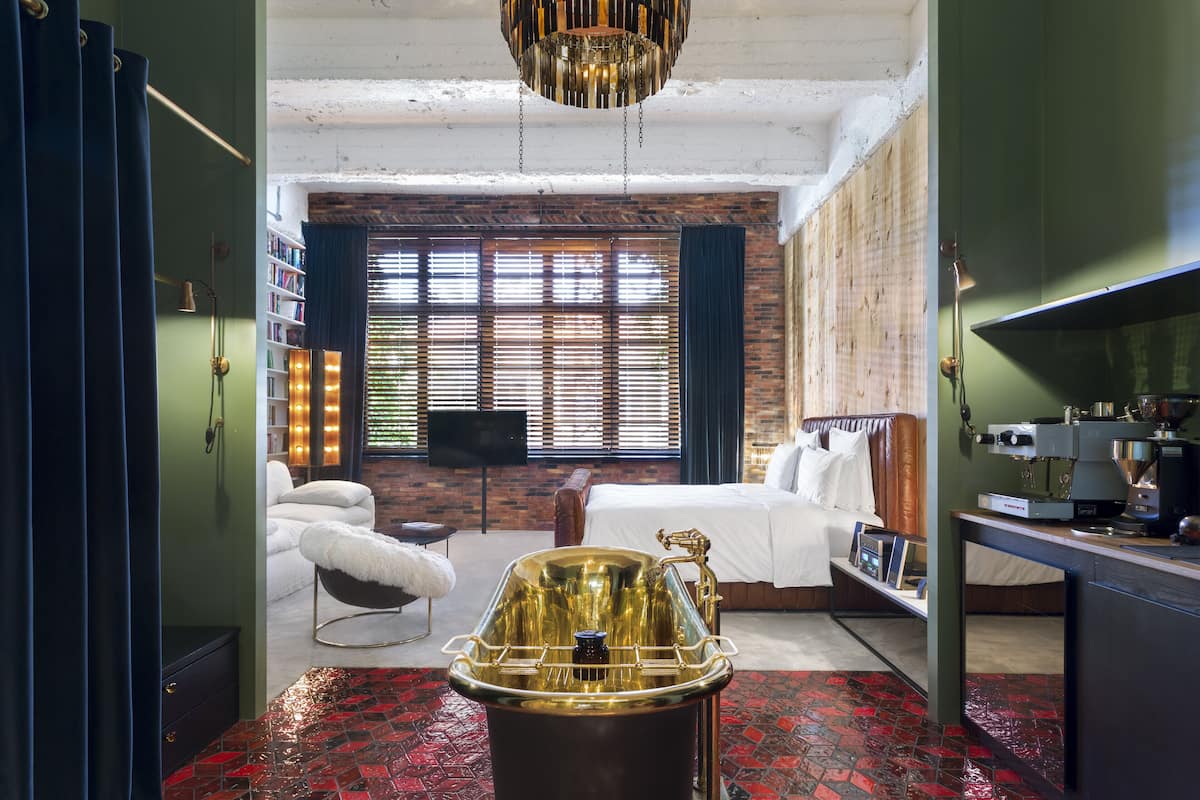 A hotel room with a large bathtub, a bed, a desk with a coffee machine, and a bookshelf.