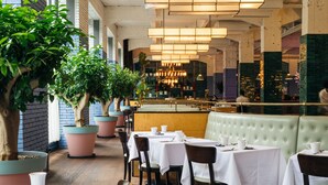 Restaurante com mesas, cadeiras, plantas em vasos e vista da cidade.