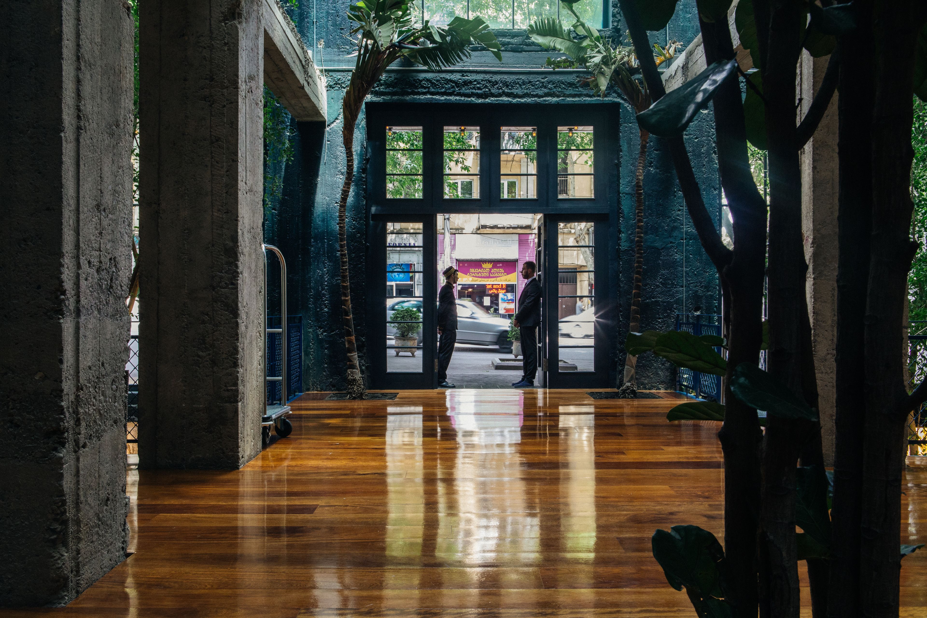An interior corridor with a polished wooden floor, large windows, and a view of the street outside.