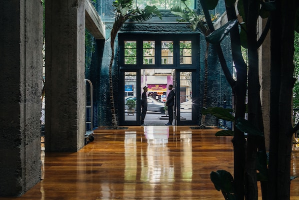 An interior corridor with a polished wooden floor, large windows, and a view of the street outside.