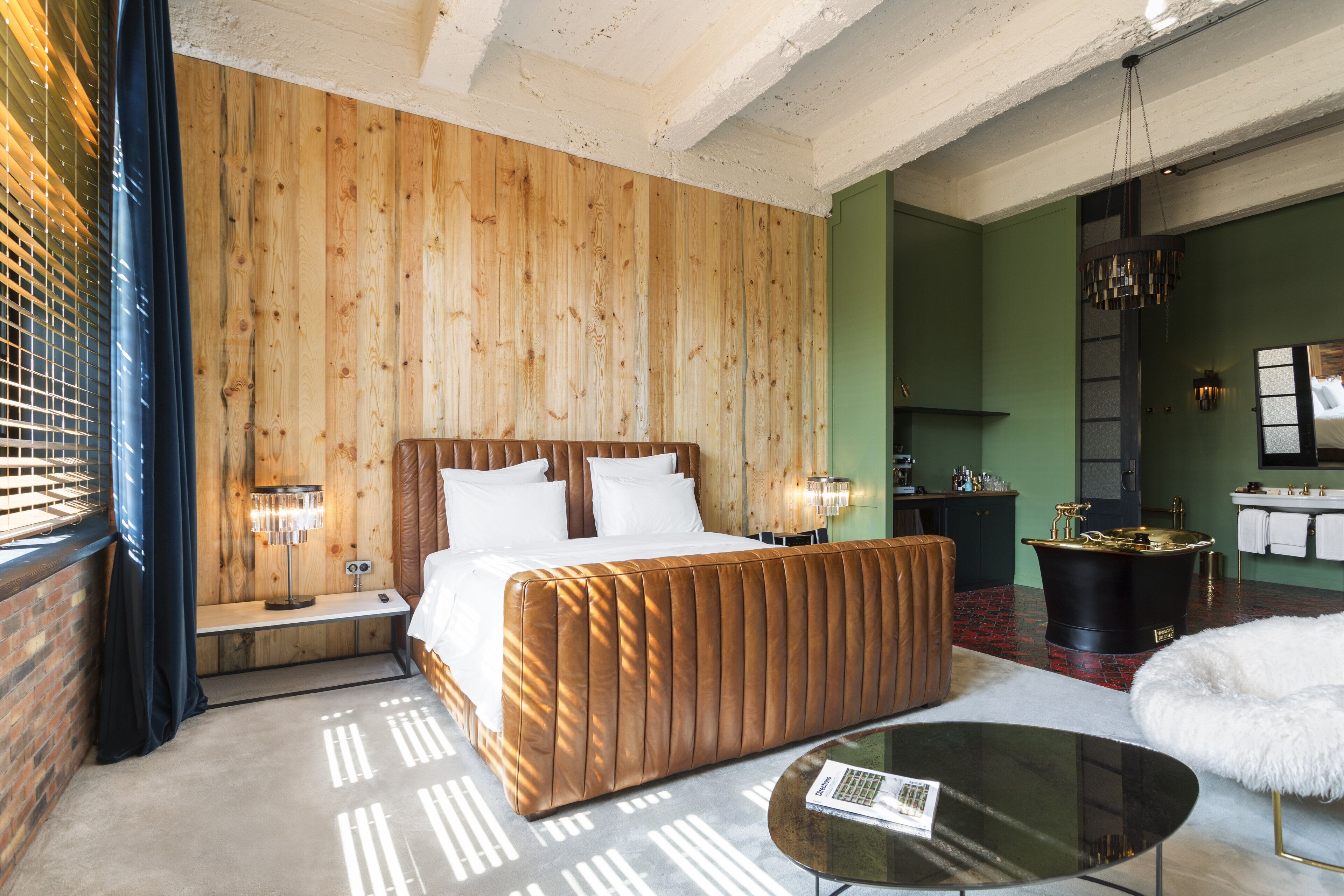 Habitación de hotel con pared de paneles de madera, una cama grande, un área de descanso con una mesa de vidrio y un baño con bañera.