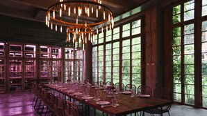 A long dining table set for a meal with chairs, large windows, and a chandelier.