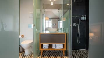 A modern bathroom with a toilet, sink, and shower. There is a glass partition, a patterned floor, and a shelf with towels.