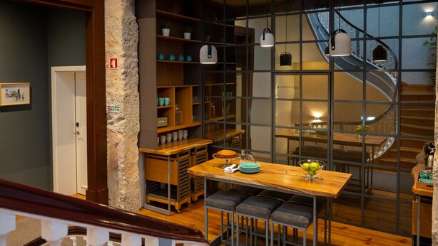 A modern interior with a wooden dining table, benches, a staircase, and a view of a cityscape through a large window. - Santa Catarina FLH Suites (Porto)