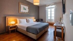 A hotel room with a large bed, bedside lamps, a small table, a TV, and a window with curtains. - Santa Catarina FLH Suites (Porto)