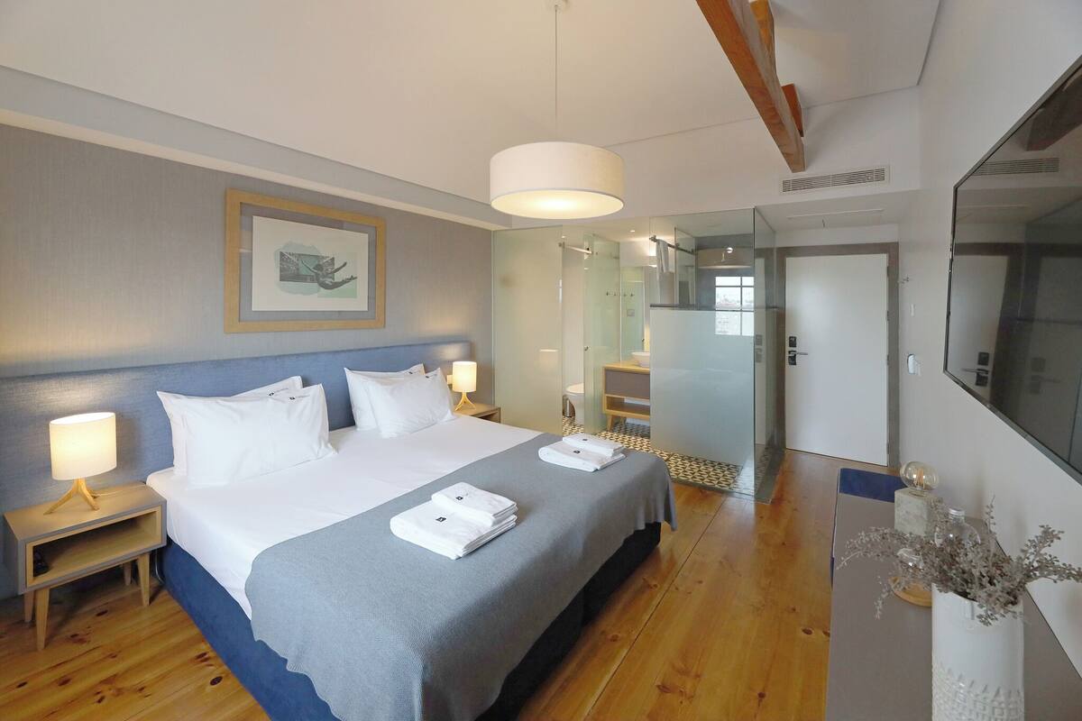 A modern hotel room with a large bed, bedside tables, a mirror, and a view into the bathroom.