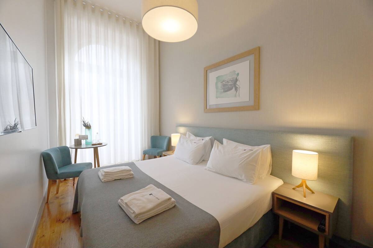 A hotel room with a bed, two chairs, a small table, a lamp, and a painting on the wall.
