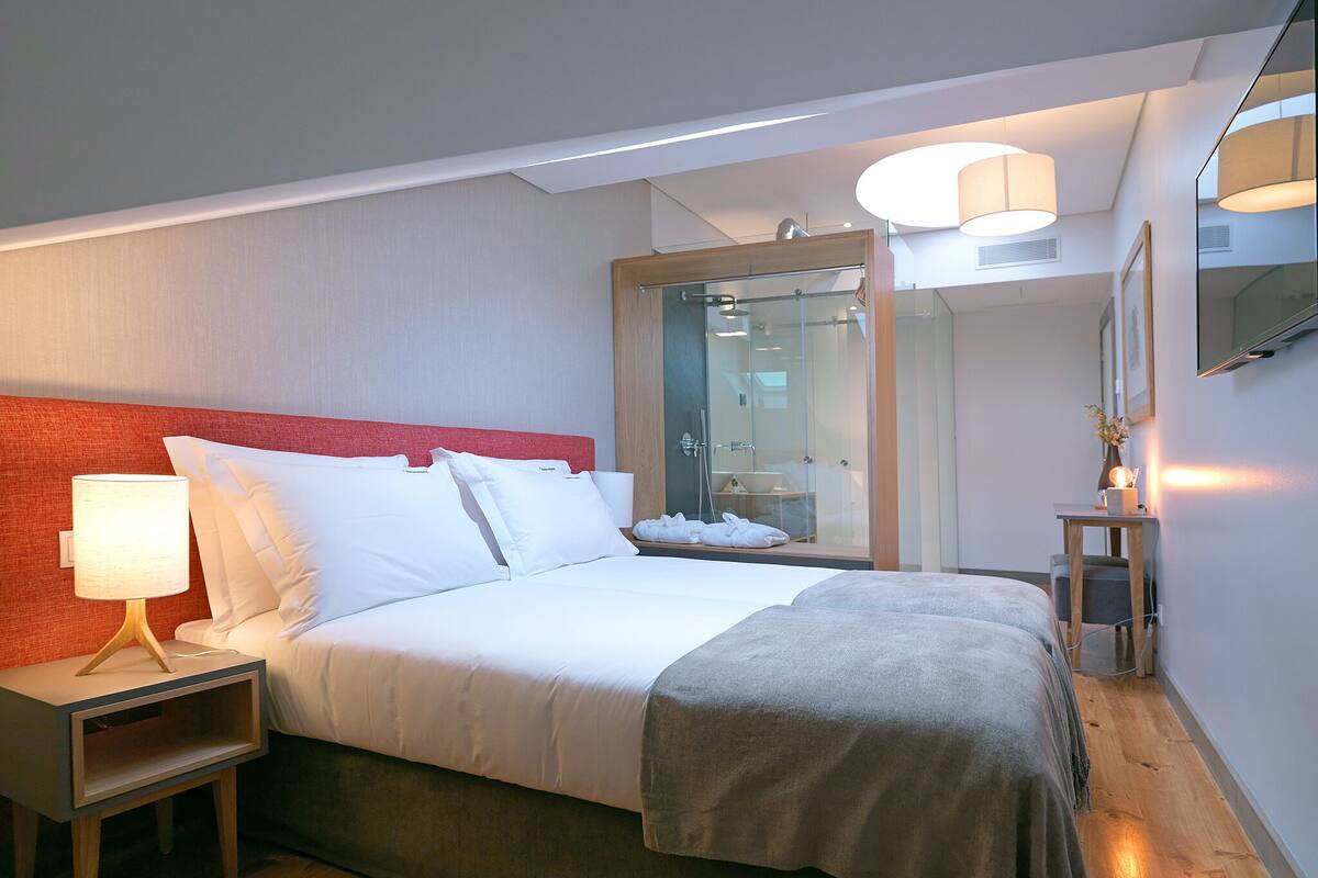 A modern hotel room with a bed, bedside table, lamp, and a large mirror.