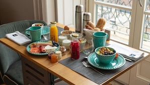 A breakfast table with various food items, a coffee maker, and a window with a view of the street. - Santa Catarina FLH Suites (Porto)