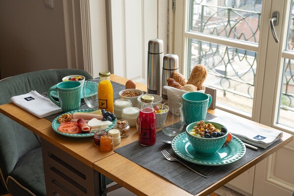 Una mesa de desayuno con diferentes alimentos, una cafetera y una ventana con vista a la calle.