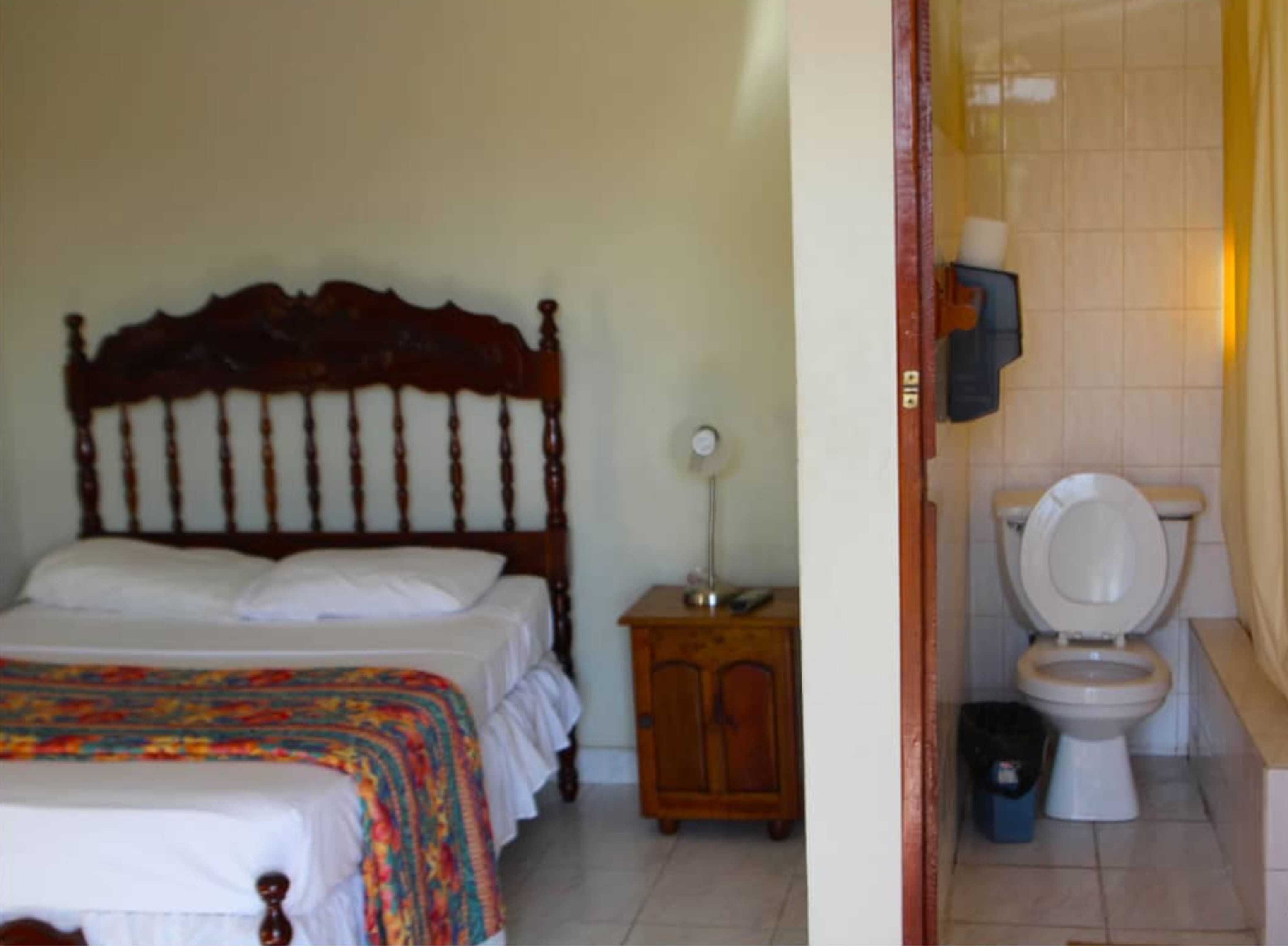 A bedroom with a wooden bed, a bedside table with a lamp, and a bathroom with a toilet and sink.