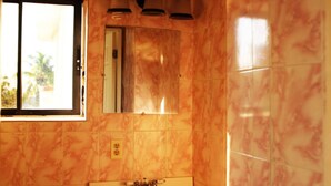 A bathroom with marble walls, a sink, and a window with a view of greenery. - Hotel Le Meridien (Les Cayes)