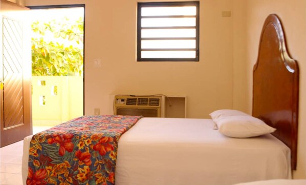 A bedroom with a bed, a window, an air conditioning unit, and a door leading to an outdoor area.