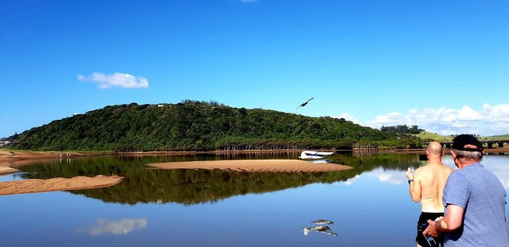Un lac paisible avec une rive sablonneuse, un bateau et une personne dans l’eau.
