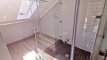 A modern bathroom with a glass shower enclosure, white tiled walls, and a wooden floor.