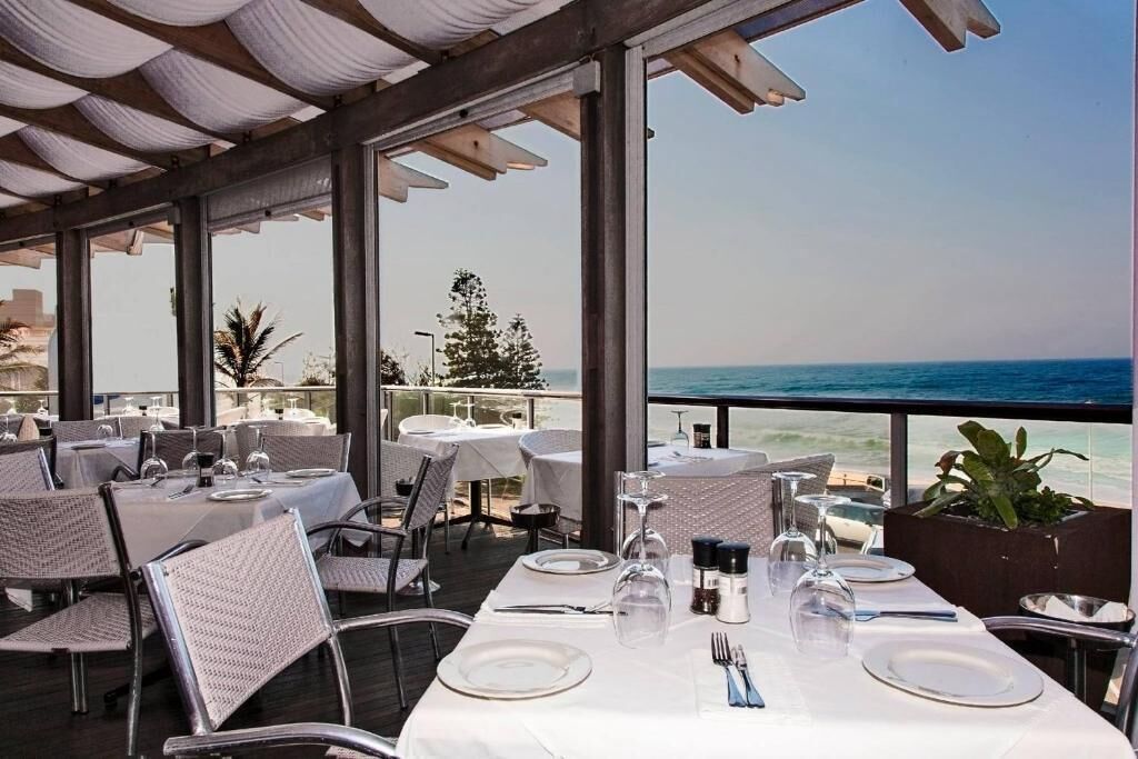 An outdoor dining area with tables set for two, overlooking a beach.