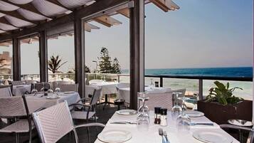 An outdoor dining area with tables set for two, overlooking a beach.
